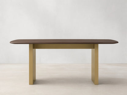 Wood dining table with a solid oak top in dark finish, supported by a rectangular base in antique brass. Placed on a wooden floor.