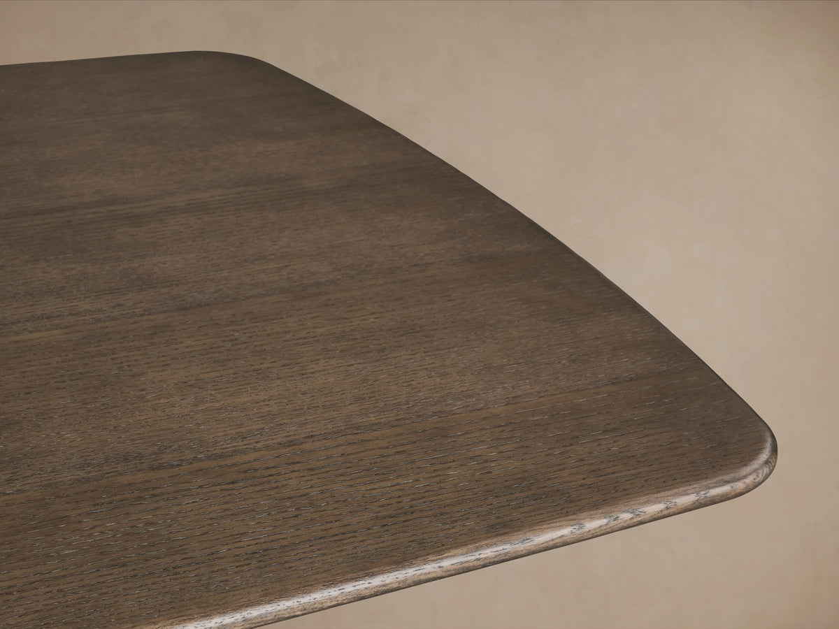 Saint Germain Wood Dining Table with dark oak top and gold steel launette base on wooden floor, neutral background.