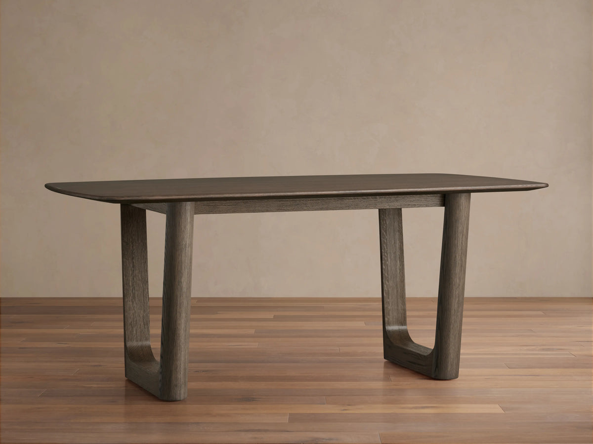 Wood dining table with rectangular top in dark finish, supported by two solid square legs, on a wooden floor background.