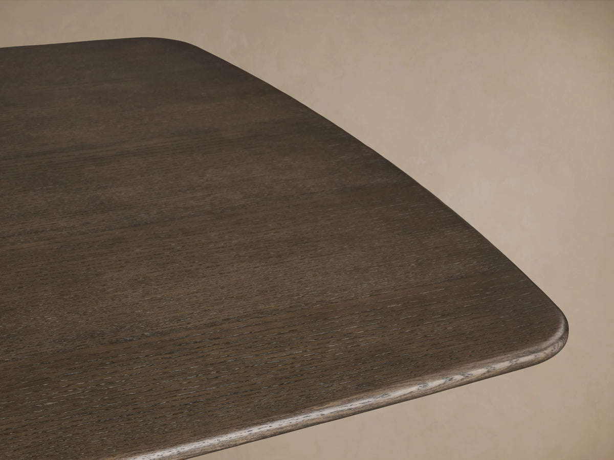 Rectangular Saint Germain Wood Dining Table with dark finish, featuring solid oak top and thick, curved legs in Ebony on a wooden floor.