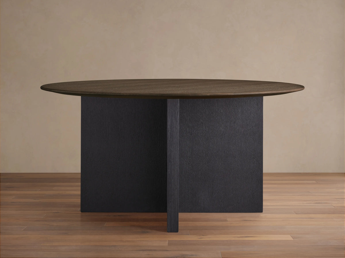 Round wooden table with a dark oak tabletop and an ebony-finished cross-shaped Clement base, on a wooden floor.