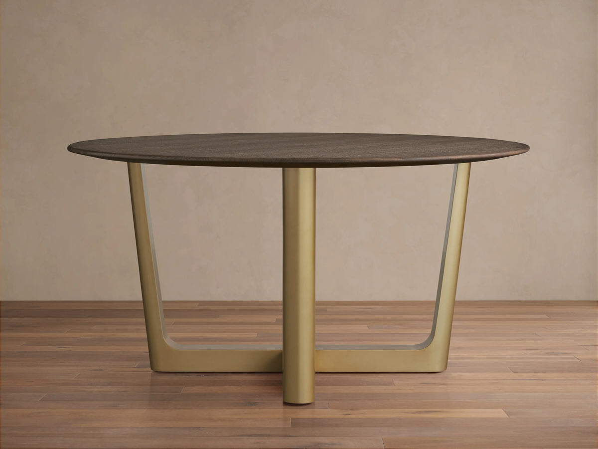 Saint Germain Round Wood Dining Table with a dark oak top on a brass-finished, cross-shaped Rennes base, set on wooden floor.