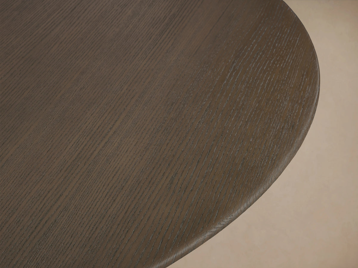 Saint Germain Round Wood Dining Table with a dark oak tabletop and a curved Rennes base in a golden finish on a wooden floor.