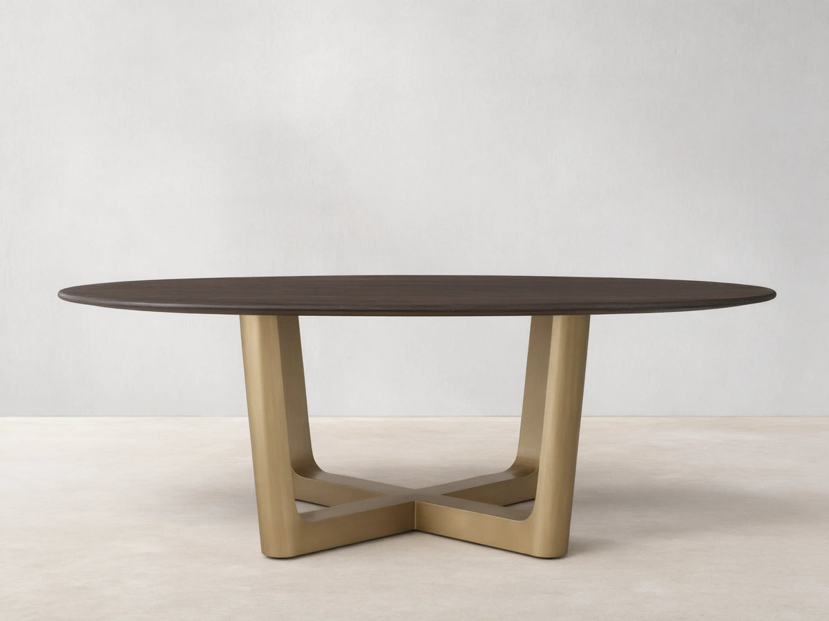 Saint Germain Round Wood Dining Table with a dark oak top on a brass-finished, cross-shaped Rennes base, set on wooden floor.