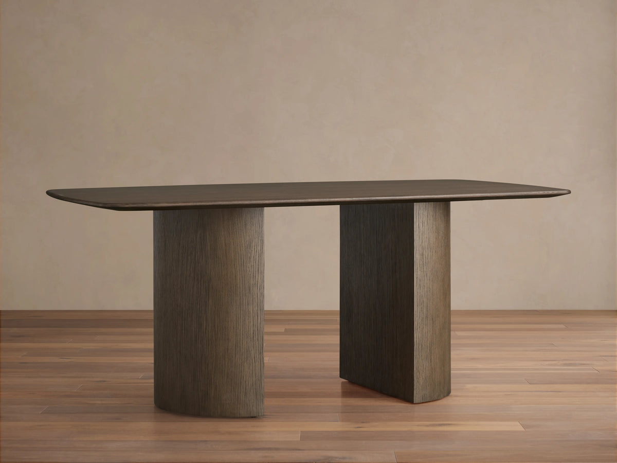 Saint Germain Wood Dining Table with rectangular top, wooden Dauphine base, dark finish, on hardwood floor, beige wall background.