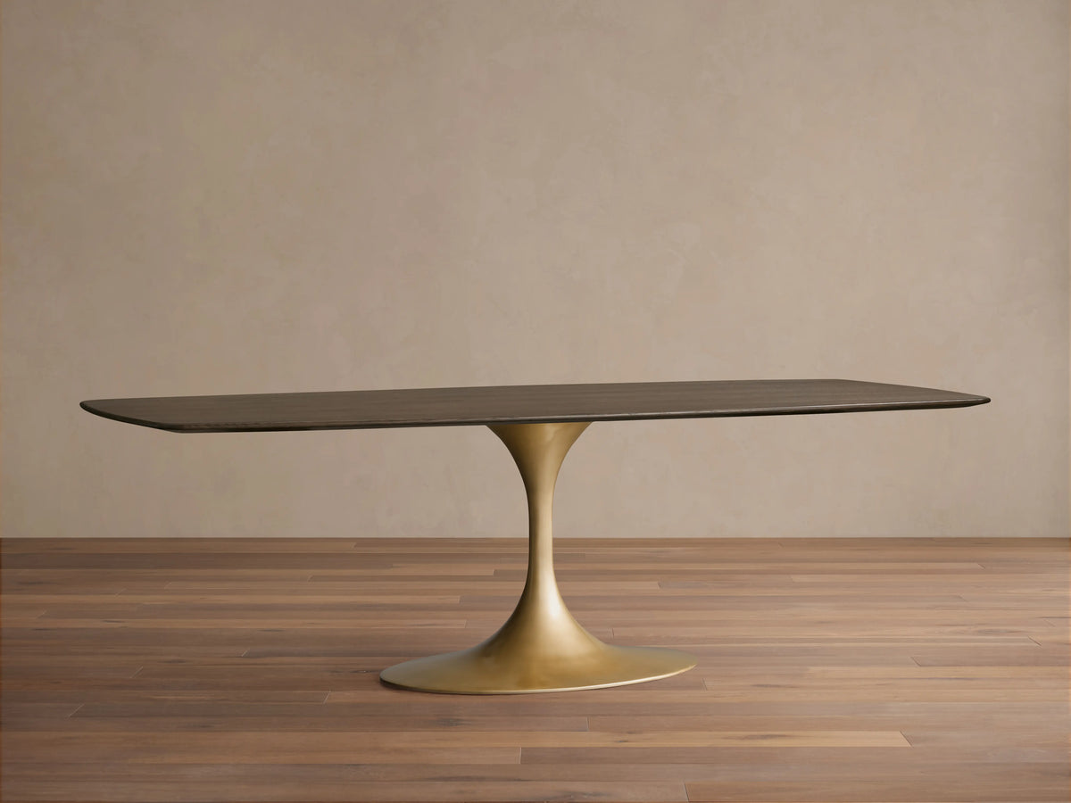 Saint Germain dining table with solid oak top in dark finish, featuring a sleek gold steel launette base on a wooden floor.