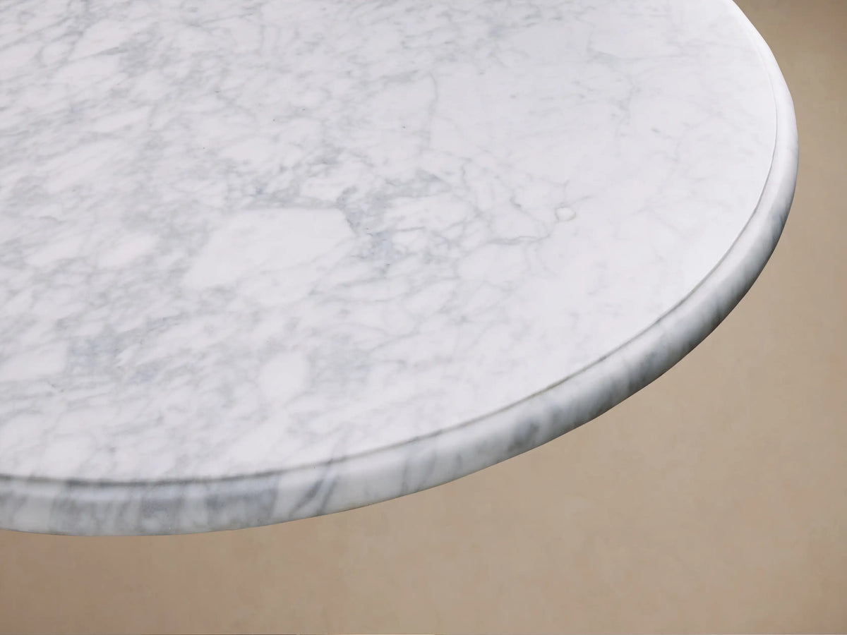 Top-down view of the circular white Carrara marble top of the Clemence Bistro Table, showing gray veining.