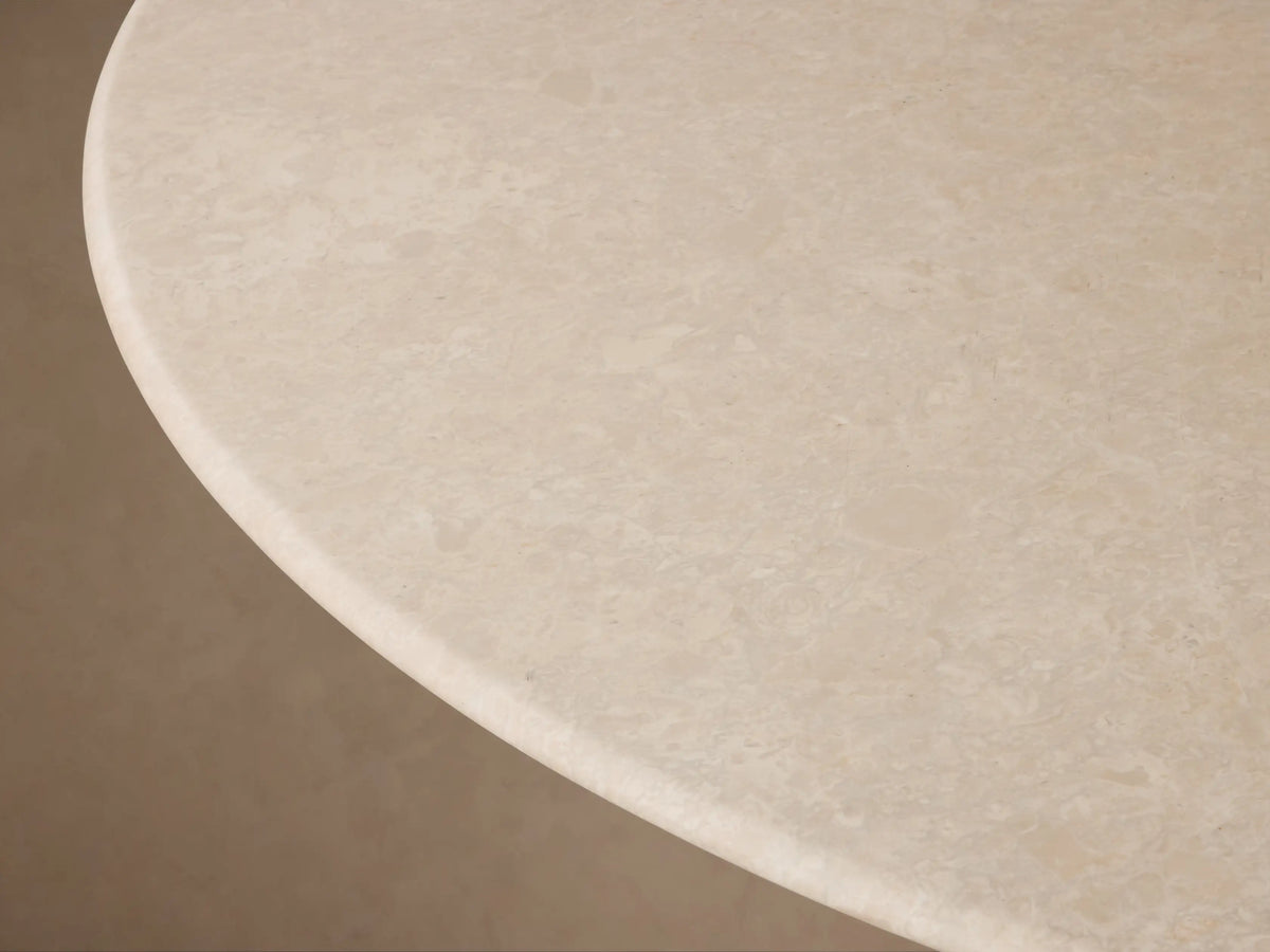 Saint Germain Round Stone Dining Table: Cream marble top, dark tapered oak base, on wood floor, tan wall.