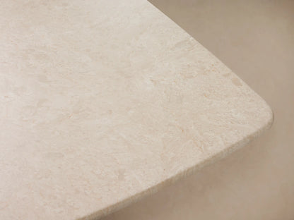Saint Germain Stone Dining Table: light cream stone rectangular top with rounded edges, dark trapezoidal base, on wood floor.