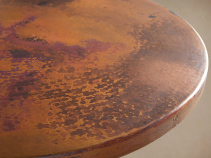 Recycled Metal Counter Table with Wade Base, featuring a round, copper-toned tabletop and a black iron pedestal base, on wooden floor.