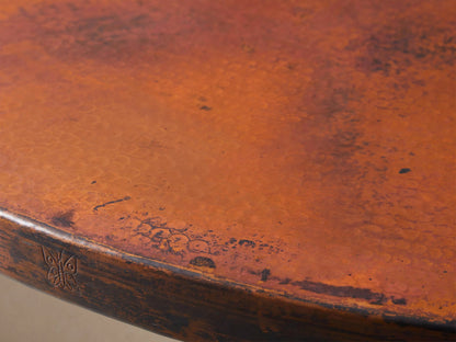Recycled Metal Bistro Table with a round, reddish-brown top and a black, ornate Wade pedestal base, on a wooden floor.