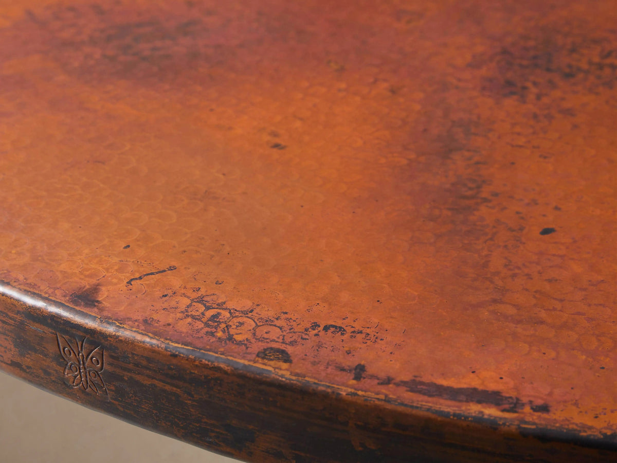 Recycled Metal Round Dining Table with Vertex Base featuring a copper tabletop with a wood grain texture; black iron base on a wood floor.