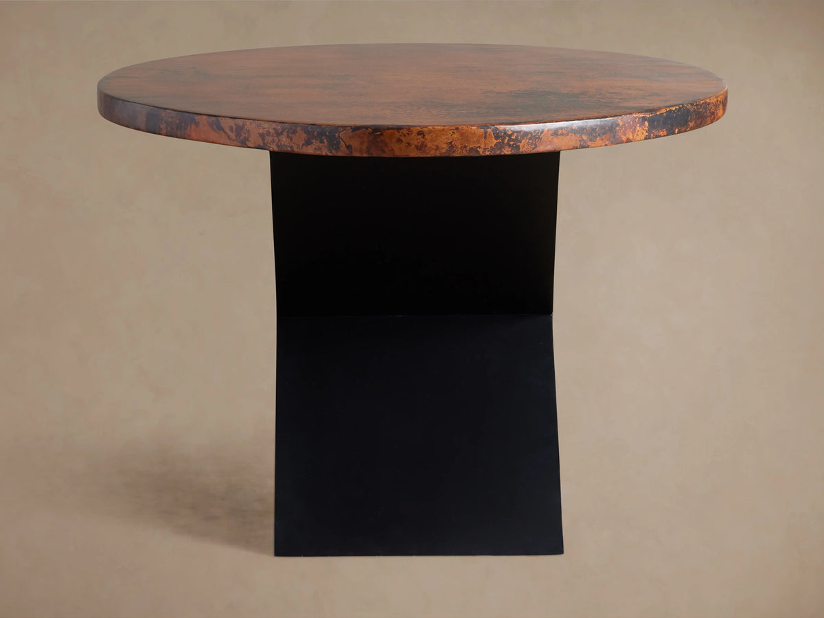 Close-up Recycled Metal Dining Table showing mottled coppery-brown textured surface with a subtle sheen & an embossed butterfly on its edge.