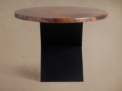 Close-up Recycled Metal Dining Table showing mottled coppery-brown textured surface with a subtle sheen & an embossed butterfly on its edge.