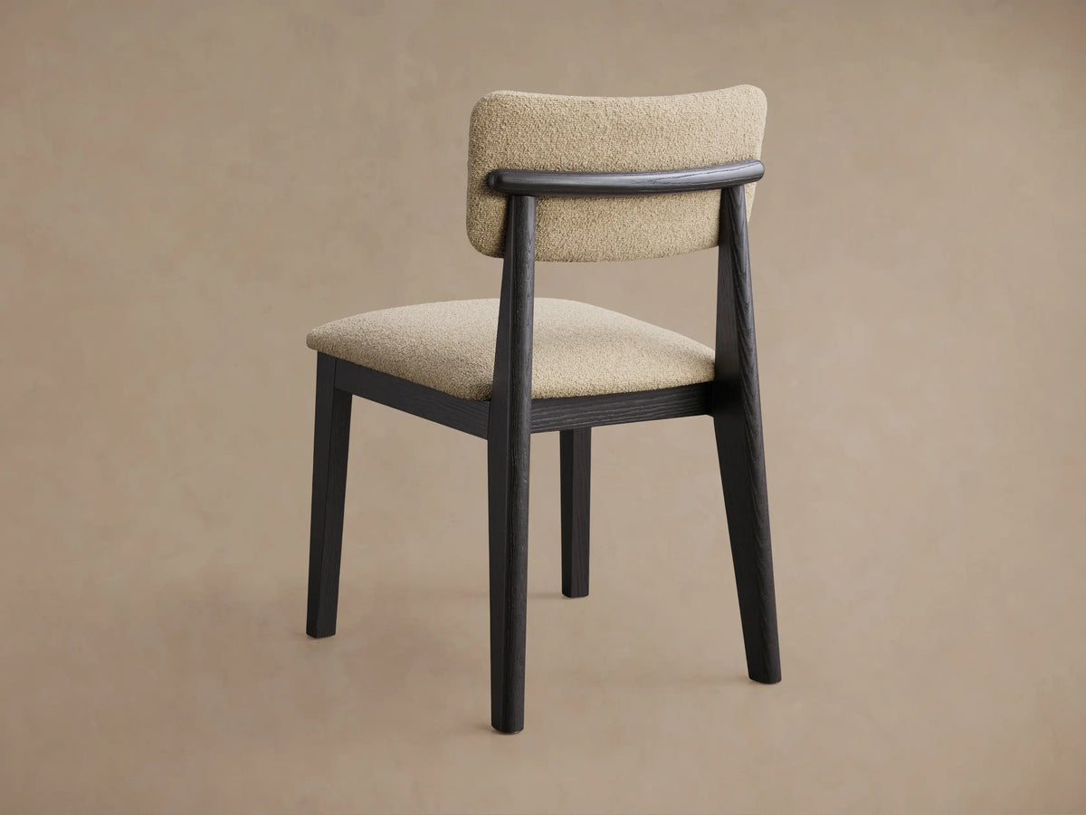 Rear view of the Corrado Dining Side Chair, showing its dark ash wood frame and light beige upholstered seat and back with a curved wood bar.