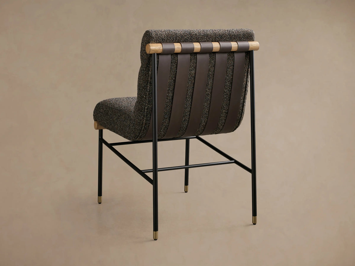 Front view of an armless accent chair featuring dark speckled boucle fabric, channel-tufted back, black metal legs with gold caps, and light wood accents.