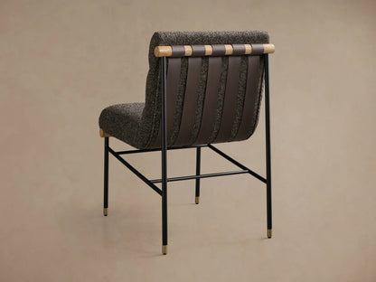 Front view of an armless accent chair featuring dark speckled boucle fabric, channel-tufted back, black metal legs with gold caps, and light wood accents.