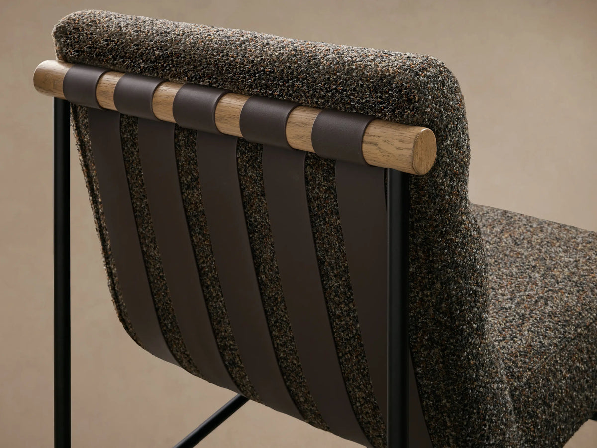 Rear view of a charcoal textured chair with brown vertical straps over wooden dowels, black metal frame, and brass-tipped legs.