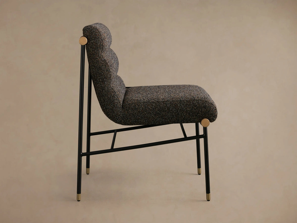 Close-up of a chair back with multi-tonal brown bouclv© upholstery, dark brown leather straps, and natural wooden dowels.
