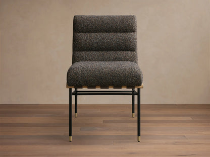 Side profile of a dark speckled upholstered lounge chair with a wavy backrest, black metal frame, and brass accents.