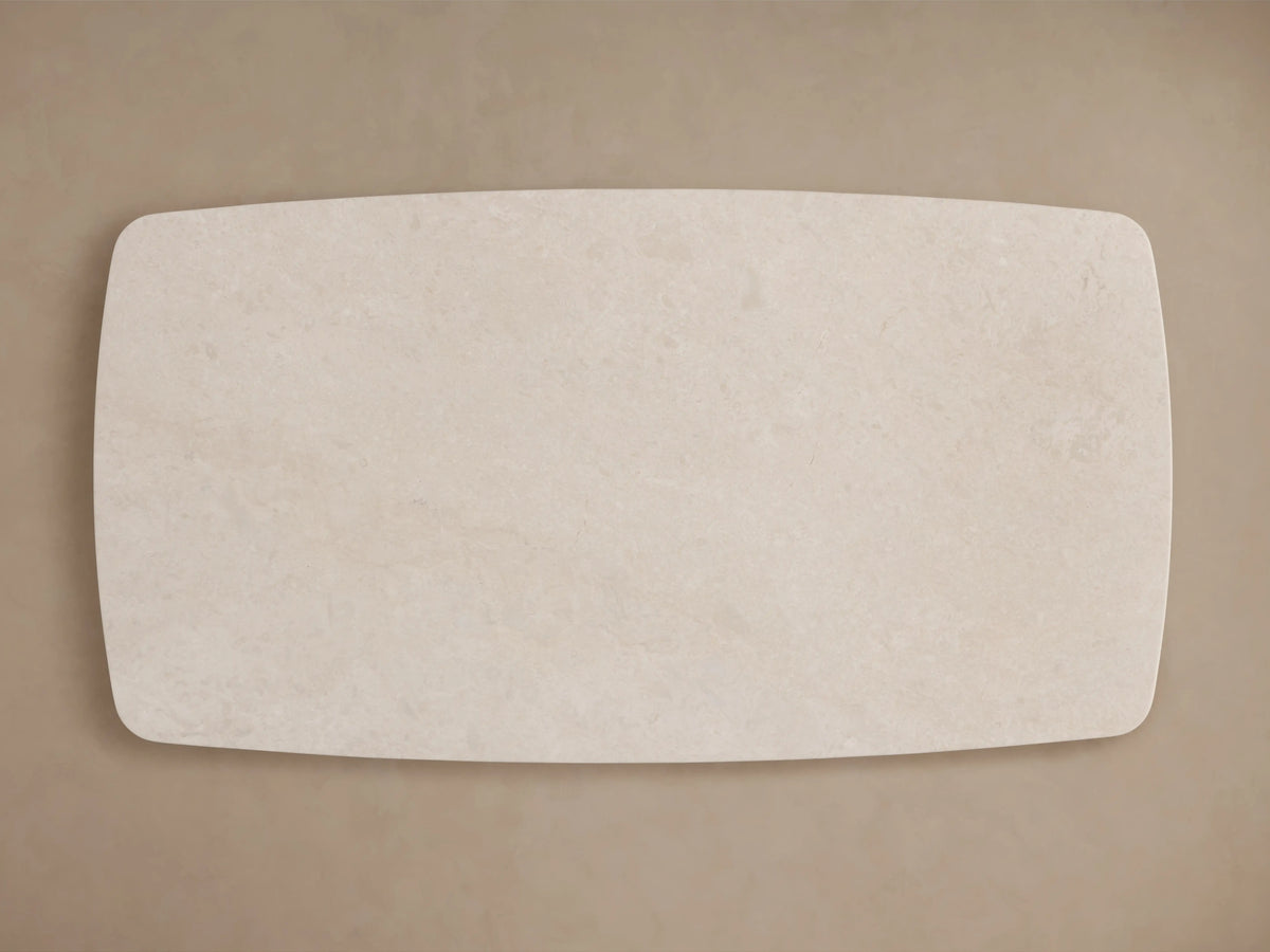 A close-up view of the Saint Germain dining table's stone tabletop, featuring cream marble with subtle veining and smooth rounded edges.