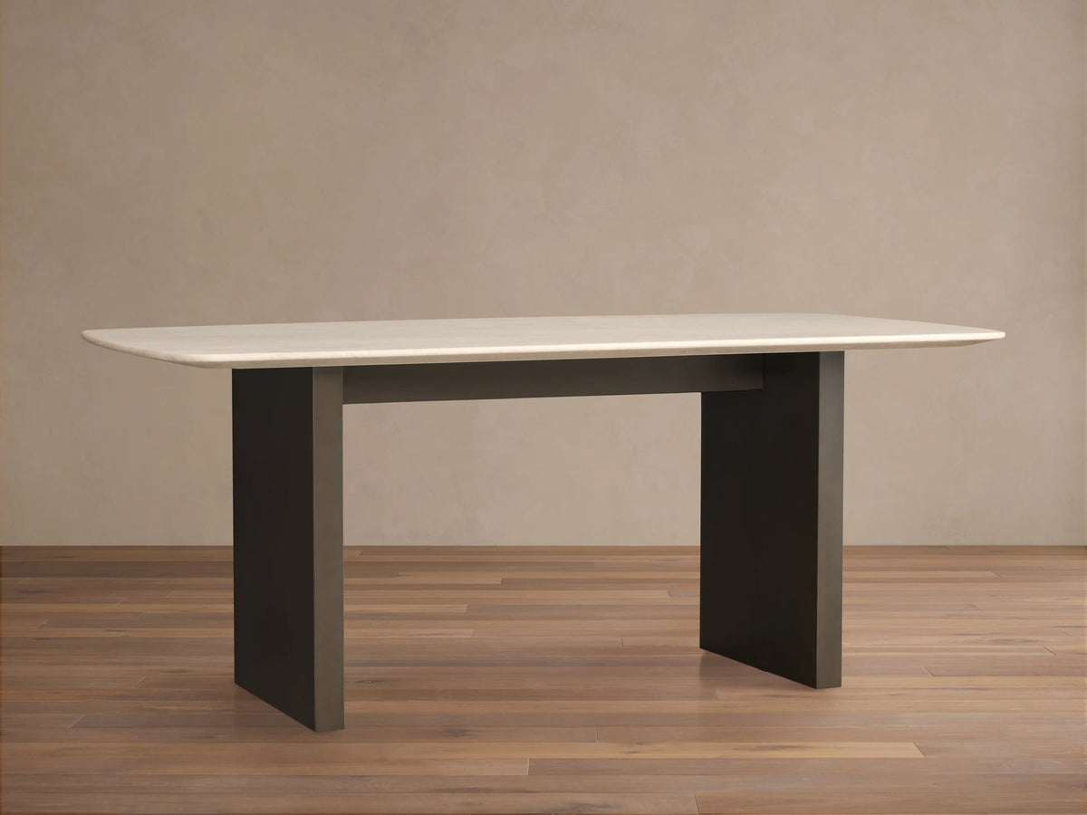 Saint Germain Stone Dining Table with cream marble top and dark wood base, rectangular shape, on a wooden floor in a neutral room.