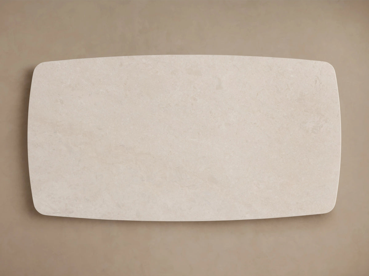 The image shows a close-up of the Saint Germain Stone Dining Table's corner. It features a smooth cream marble tabletop with subtle veining, set against a beige background.