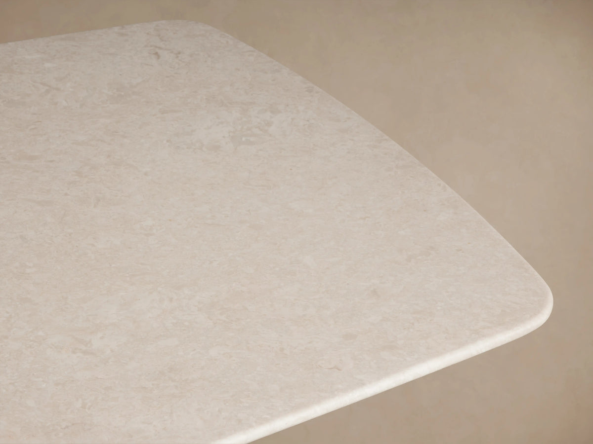 Saint Germain dining table with a cream marble top and dark ebony wood base, on a wooden floor, against a beige wall.