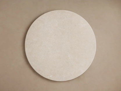 Round marble tabletop with a cream-colored surface, displaying natural patterns and subtle veining, viewed from a side angle.