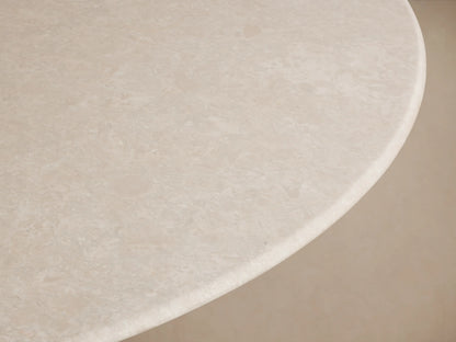 Round dining table with a smooth white stone top and a sturdy, rectangular dark base. Placed on a wooden floor with a plain beige background.