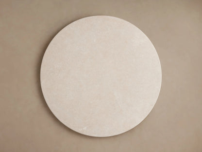 Round dining table with Carrara marble top and gray trapezoidal base on a wooden floor, against a beige background.