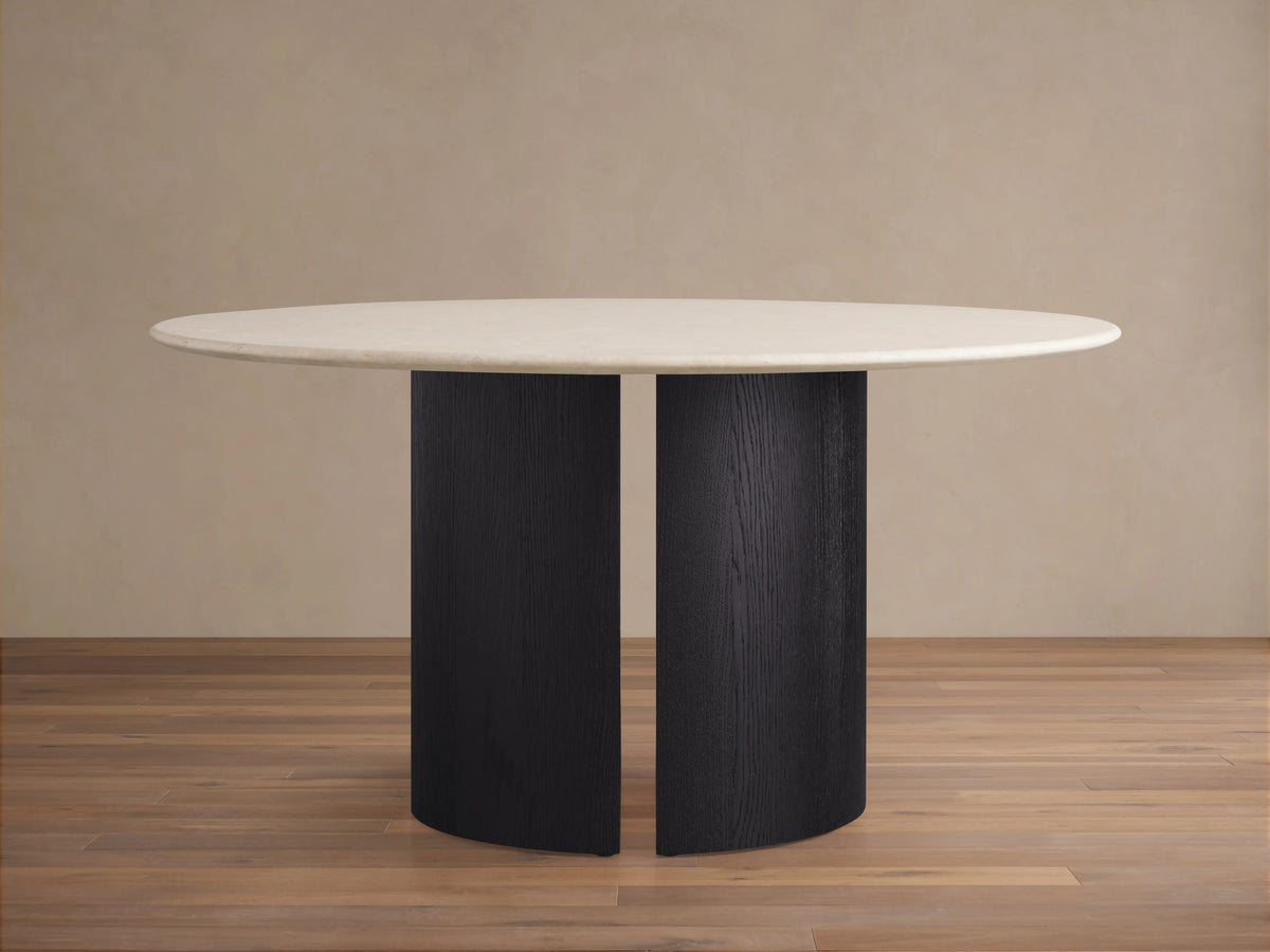 Round dining table featuring a cream marble top and a Dauphine base with a dark oak veneer finish, set on a wood floor.