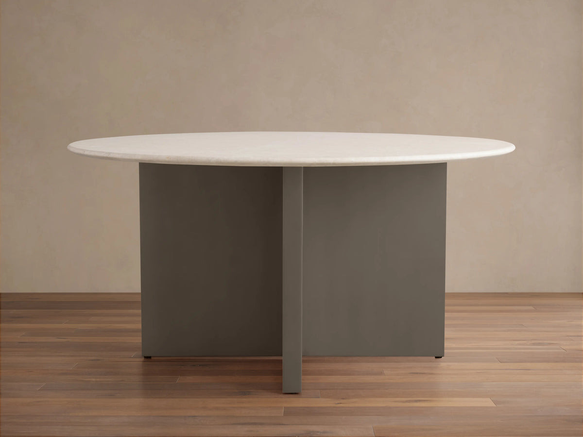 Round dining table with a light stone top, featuring a minimalist base with intersecting dark panels, on a wooden floor.