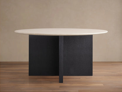 Round dining table with a light stone tabletop and dark wood base in a cross shape. Set on a wooden floor against a neutral wall.