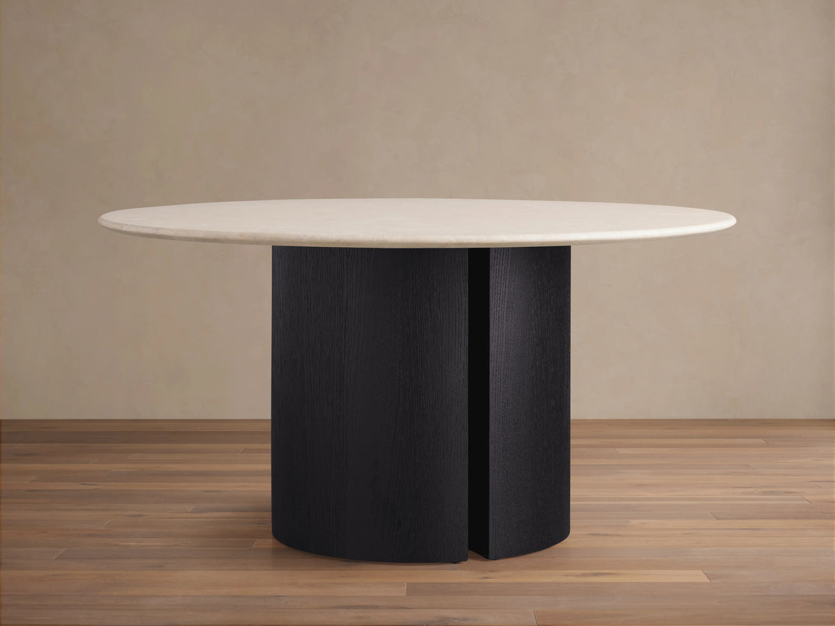 Round dining table with a smooth cream stone top and dual vertical dark ebony base on a wooden floor background.