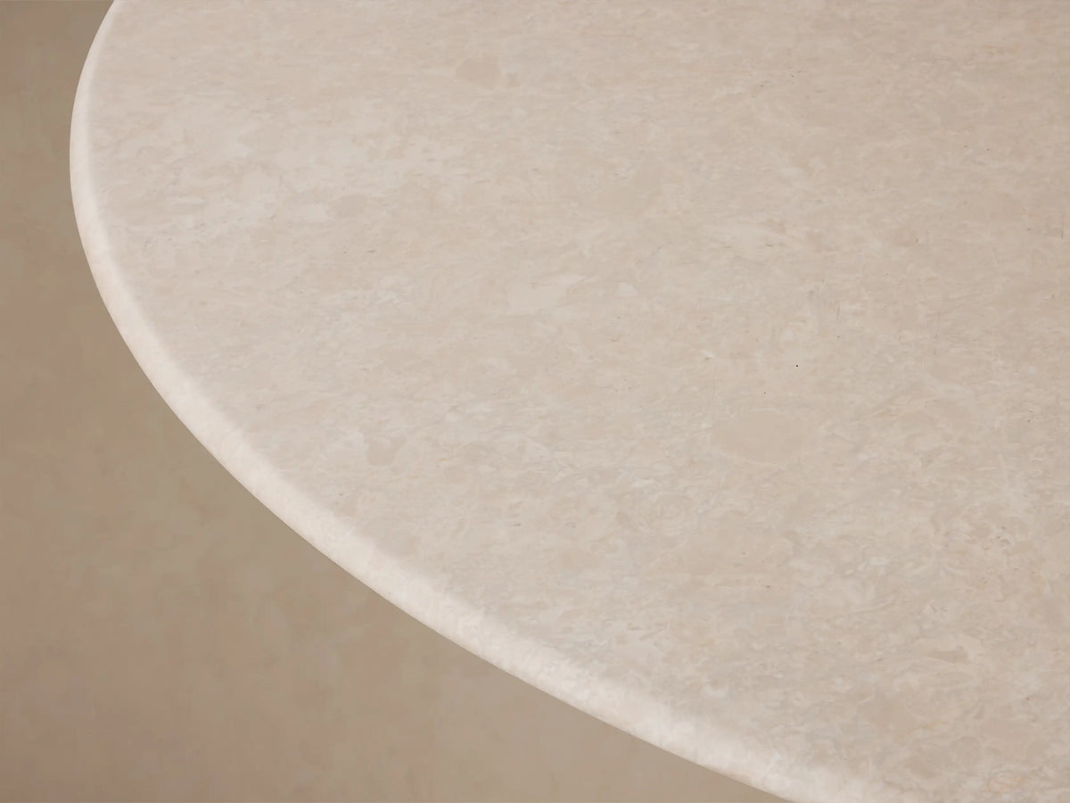 Front view of the Saint Germain Round Stone Dining Table with Launette Base, featuring a light stone round top and a dark bronze hourglass-shaped steel base.