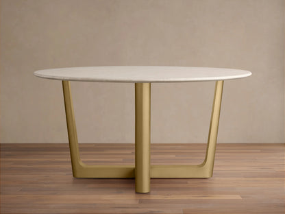 Round dining table with a white Carrara marble top on a brass-finished steel Rennes base, in a simple room with wooden flooring.