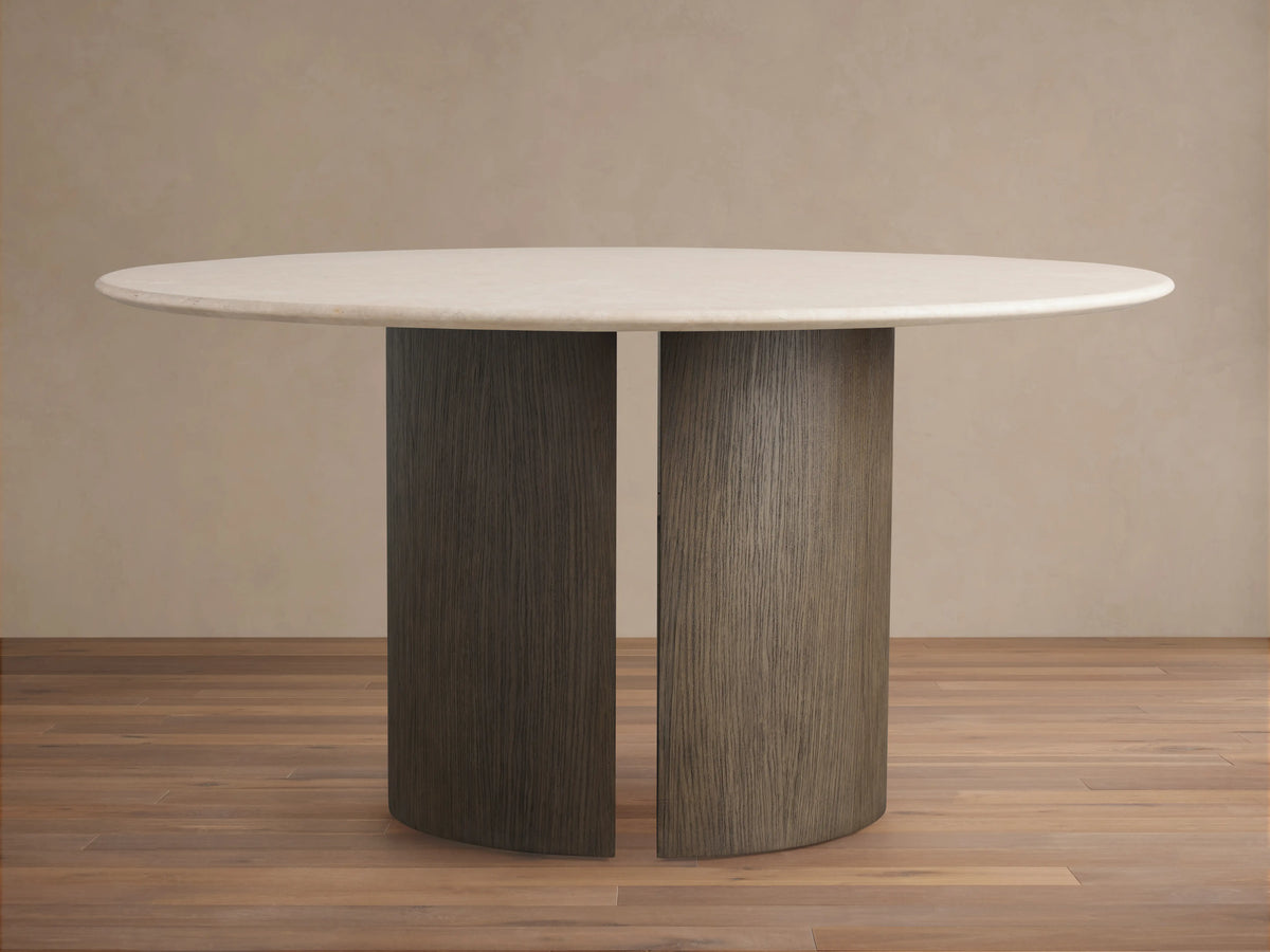 Round dining table with a cream marble top and a dark wood veneer base, set on a wooden floor against a beige wall.