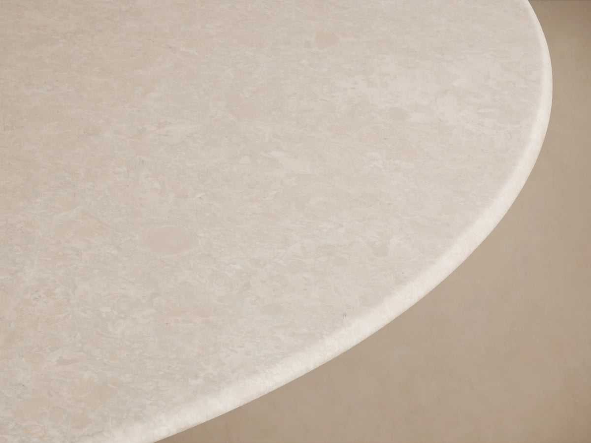Saint Germain Round Stone Top Dining Table with a cream marble top and a dark wooden rectangular base on a wood floor background.