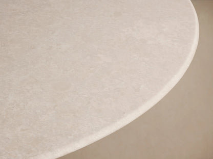 Round dining table with a cream marble top and a Rennes base crafted from steel in an antique brass finish, set on a wood floor.