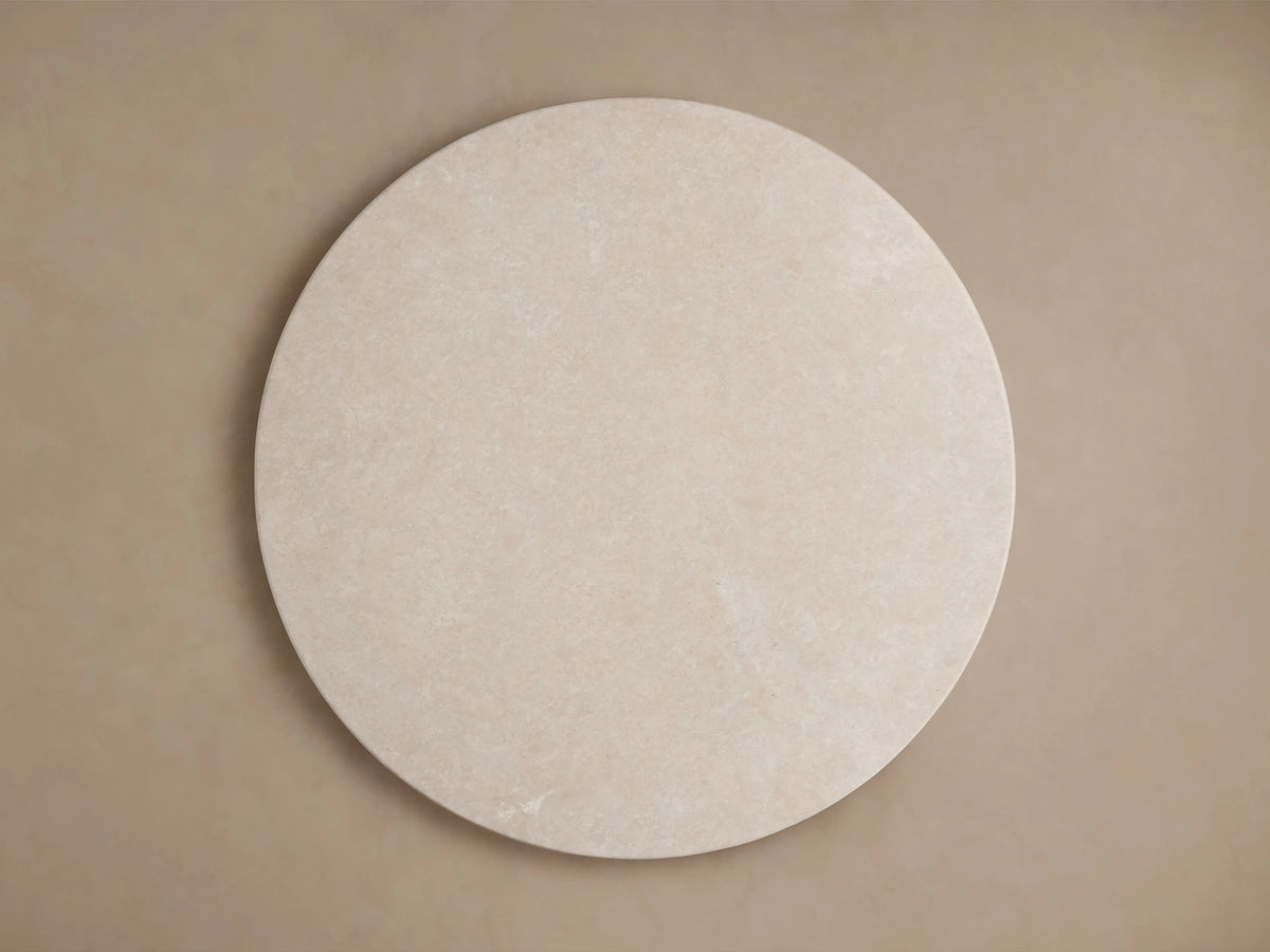 Round dining table corner in light cream stone with subtle marbling. Smooth surface and thin edge visible from top angle.