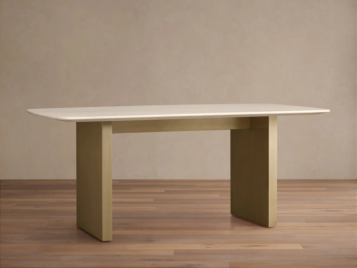 Saint Germain Stone Dining Table with cream marble top, elegant rectangular shape, and gold steel base on a wooden floor background.