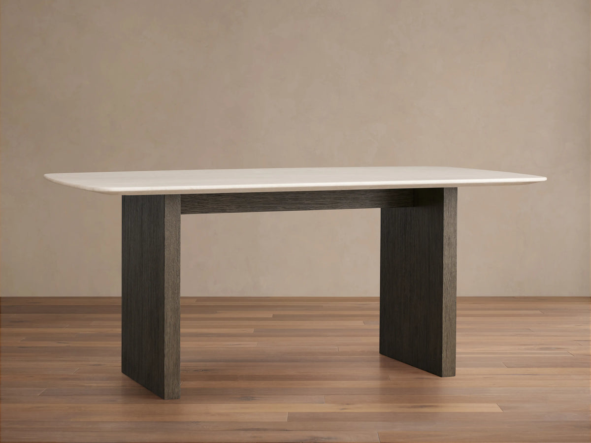 Saint Germain dining table with a cream stone marble top and dark wood base on a wood floor, against a neutral wall.