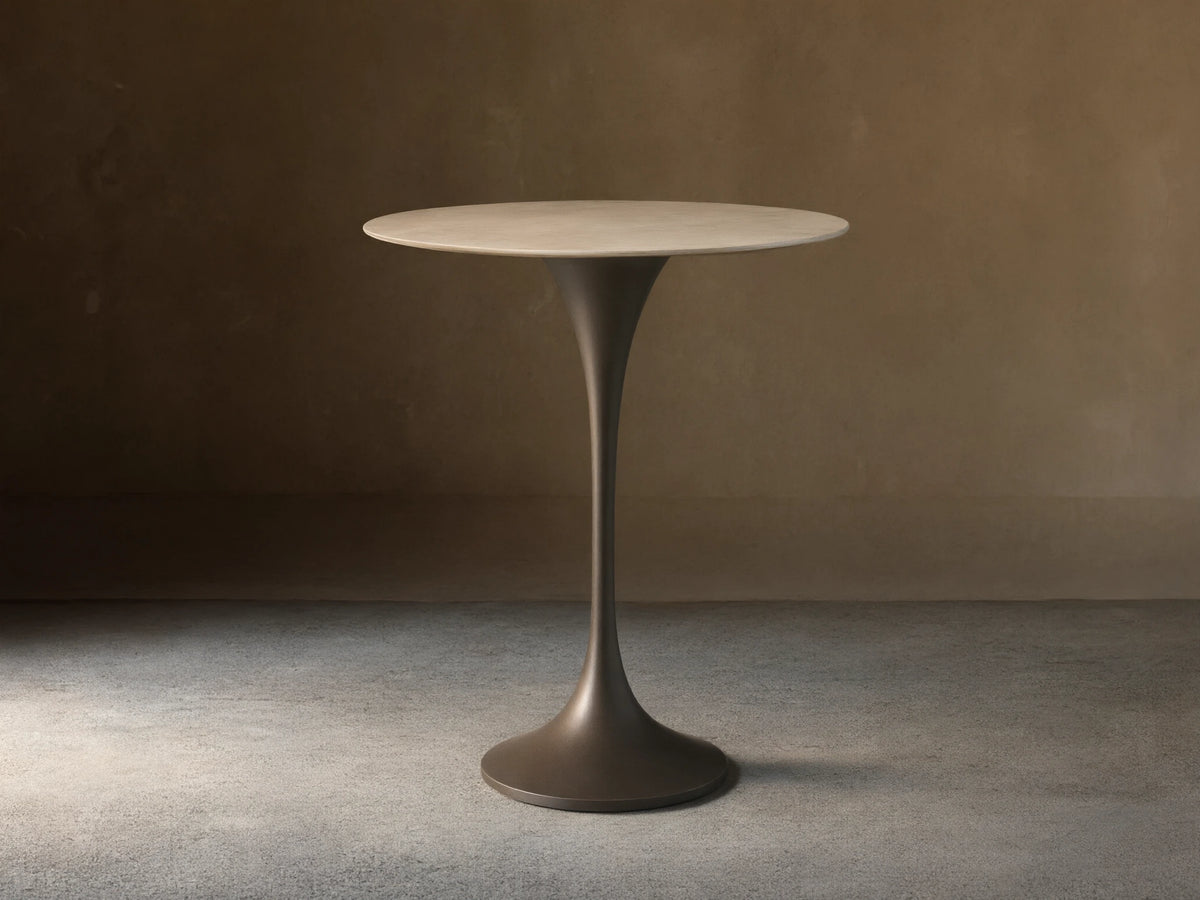 Front view of Saint Germain Counter Table with a round light stone top and dark trumpet-shaped steel base.