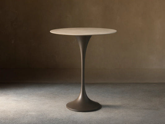 Front view of Saint Germain Counter Table with a round light stone top and dark trumpet-shaped steel base.
