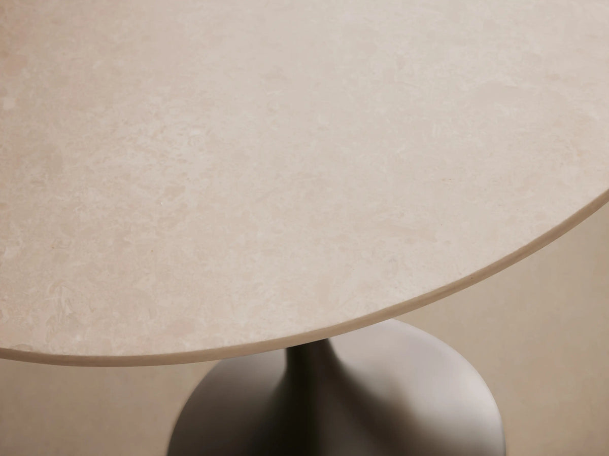 Saint Germain Bistro Table with a round cream marble top and sleek steel base, set on a wooden floor against a beige wall.