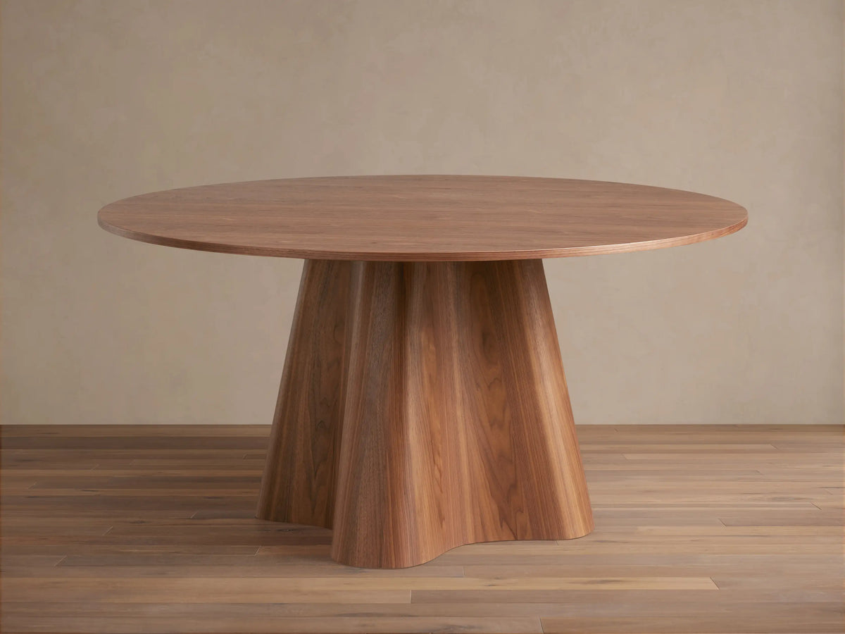 Round wooden dining table with a smooth top and a unique, flared pedestal base. Light brown finish on wood grain.