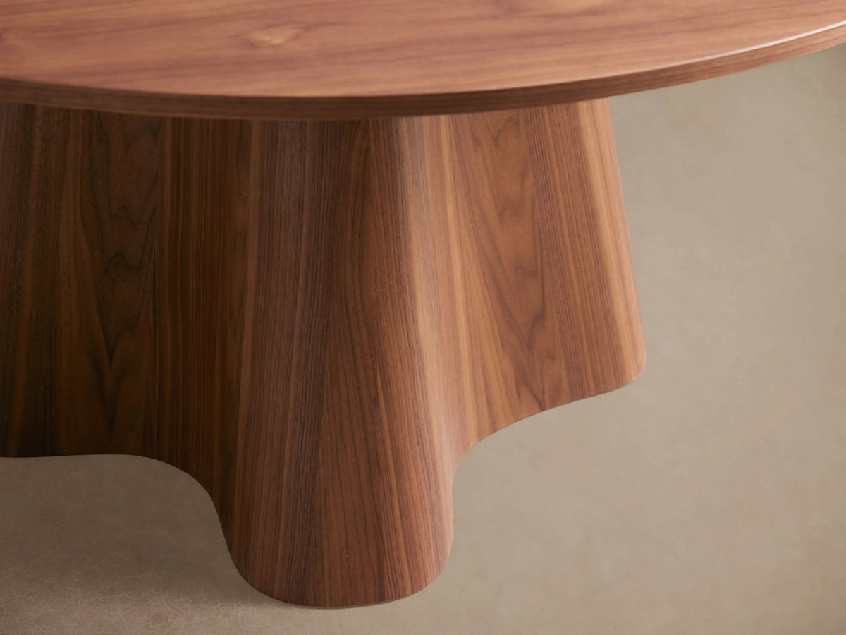 Round wooden dining table with a smooth top and a unique, flared pedestal base. Light brown finish on wood grain.