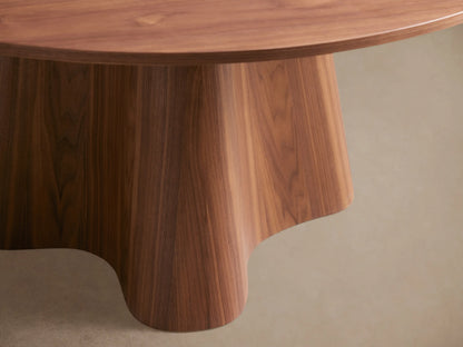 Round wooden dining table with a smooth top and a unique, flared pedestal base. Light brown finish on wood grain.