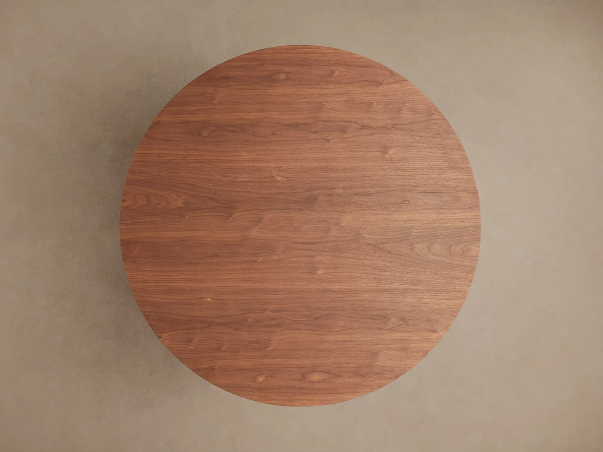 Cortina Round Dining Table with smooth, wood finish, showing the elegant curves of its base and round tabletop in warm brown tone.